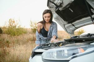 Attractive slim young girl in summer shorts and shirt repairs a broken car. A beautiful woman stands near raised car hood. photo