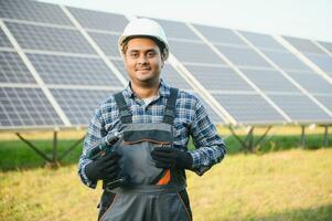 Indian man in uniform on solar farm. Competent energy engineer controlling work of photovoltaic cells photo
