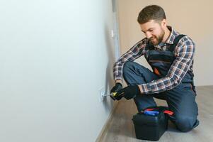 Electrician with screwdriver repairing power socket in room photo