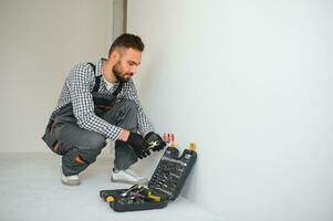 Electrician in uniform mounting electric sockets on the white wall indoors photo