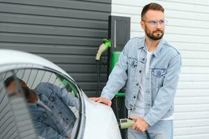 elegante hombre inserta enchufe dentro el eléctrico coche cargando enchufe foto