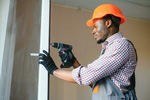 de cerca de joven africano personal de mantenimiento en uniforme instalando ventana foto