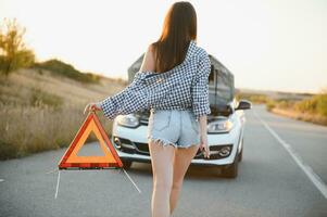 Beautiful sexy woman holding an emergency stop sign near a broken car. photo