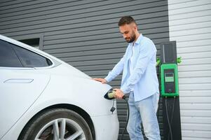 Man charging electric car by the house. photo