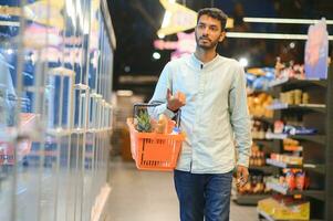 Portrait of happy Indian man standing in front of the product counter in a grocery store. Man buying grocery for home in supermarket. photo