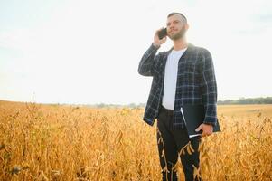 A cute farmer is standing in a soybean field and talking on the phone with his business partner photo