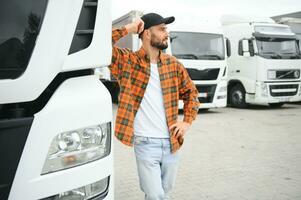 Portrait of young bearded man standing by his truck. Professional truck driver standing by semi truck vehicle. photo