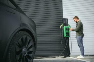 A man stands near a charging station and charges his electric car photo