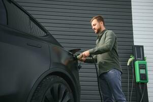 A man stands near a charging station and charges his electric car photo