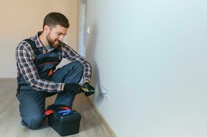 Electrician with screwdriver repairing power socket in room photo