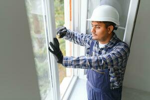 Indian Workman in overalls installing or adjusting plastic windows in the living room at home photo