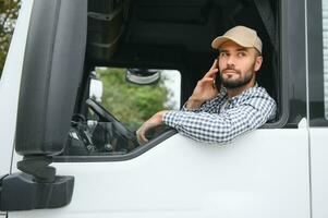 A driver sitting inside the semi-truck while looking through the open window with multiple trucks parked in the background photo