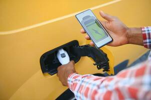 A african american man stands next to yellow electric delivery van at electric vehicle charging stations photo