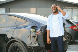 Happy young man with mobile phone charging car at electric vehicle charging station photo