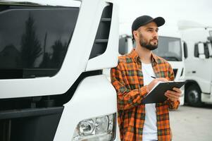 Portrait of young bearded trucker standing by his truck vehicle. Transportation service. Truck driver job photo