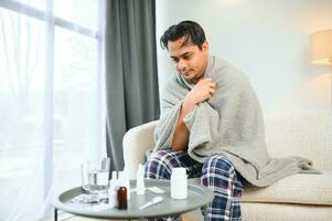 health, cold and people concept - sick young indian man in blanket having headache or fever at home photo