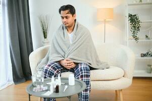 health, cold and people concept - sick young indian man in blanket having headache or fever at home photo