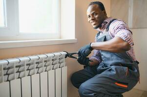 afro reparador en mono utilizando herramientas mientras instalando o reparando calefacción radiador foto