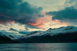 AI generated a breathtaking view of snow-capped mountains beside a tranquil lake under a vibrant, colorful evening sky. photo