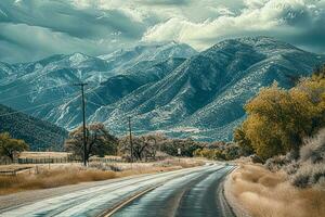 AI generated A picturesque scene of a winding road leading towards snow-capped mountains, surrounded by autumn foliage under a dramatic cloudy sky. photo