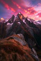 AI generated A breathtaking sunset over jagged mountain peaks adorned with snow, foreground of rocky terrain and lush grass. photo