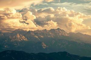 AI generated A breathtaking view of rugged mountains under a sky filled with golden, fluffy clouds illuminated by the warm hues of the setting sun photo