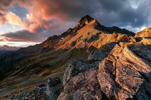 AI generated A breathtaking sunset illuminating a rugged mountain peak, casting golden hues on the rocky terrain under a dramatic cloudy sky photo