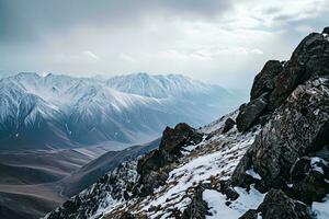 ai generado un asombroso ver de nevadas montañas, rocoso primer plano debajo un dramático nublado cielo, exhibiendo de la naturaleza grandeza. foto