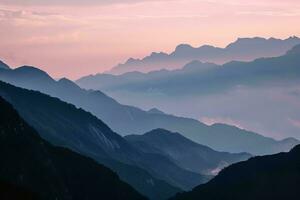AI generated a breathtaking image of layered mountains veiled in mist, under the soft glow of a tranquil sunset. The muted colors and gentle light create a peaceful and calming photo