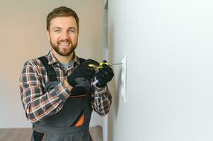 Confident professional electrician in uniform using screwdriver while replacing a socket in apartment after renovation work. photo