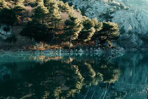 AI generated a serene lake surrounded by lush green trees and rocky terrain. The water in the lake is calm and clear, reflecting the surrounding landscape perfectly. photo