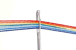 multicolor hilos para de coser en el formar de un arco iris pasar mediante un antiguo aguja en un blanco antecedentes foto