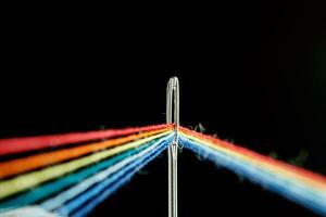 multi-colored threads for sewing in the form of a rainbow pass through an antique needle on a black background photo