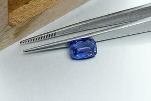 macro mineral faceted stone sapphire with tweezers on a gray background photo