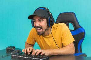 Excited handsome young male gamer playing online game on computer isolated on blue background photo