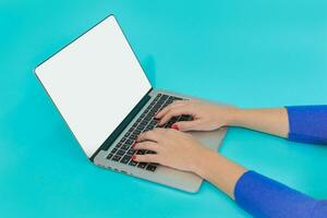 Woman hands using laptop with blank display on blue background. Modern workspace concept. Flat lay photo