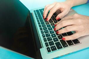 Woman hands close up using laptop with black display on blue background. Modern workspace concept. photo