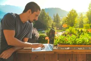 Young man working with laptop on beautiful scenic mountain background. Attractive man working. Freelancer. Traveler. photo