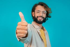 Young man doing happy thumbs up gesture with hand standing over isolated blue background. photo