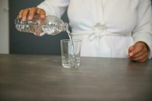 Close-up female hands pouring mineral water from a bottle into a drinking glass. Body and health care concept photo