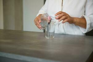 Close-up hands of woman holding glass of refreshing water, standing at kitchen island in modern minimalist home interior photo