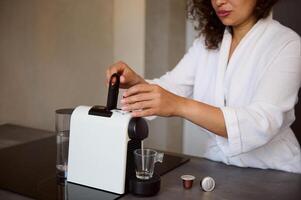 Details on hands of young woman inserting a capsule with grinded coffee inside a coffee machine for home use photo