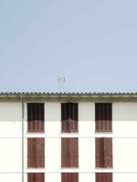 Traditional white Mediterranean-style house with wooden shutters, surrounded by greenery under a clear sky. photo