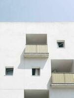 Minimalist urban architecture, white building facade with geometric balconies and windows against a clear sky. photo