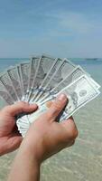 Hands holding US dollars on tropical beach. Close up video