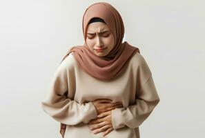 ai generado asiático musulmán mujer en hijab con manos participación estómago con dolor facial expresión aislado blanco antecedentes foto