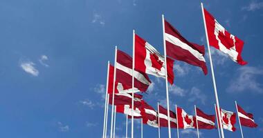 Lettonia e Canada bandiere agitando insieme nel il cielo, senza soluzione di continuità ciclo continuo nel vento, spazio su sinistra lato per design o informazione, 3d interpretazione video