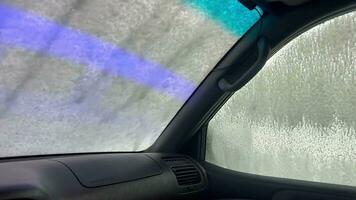 Robot car wash. Operation of an automatic foam car wash system. A colorful short video of soaping a car at a car wash. Soap solution on car glass.