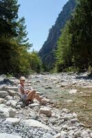 niña turista descansando en el rocas cerca el río en contra el fondo de el bosque y montañas foto