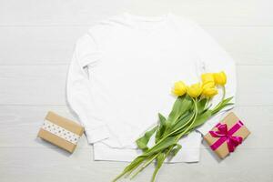 Closeup white blank template sweatshirt hoodie copy space. Mothers women day yellow tulips, gifts. Happy birthday top view mockup pullover. White wooden background. Casual outfit. Flat lay templates photo
